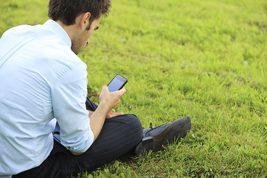 Male checking his phone while sitting on the grass Male checking his phone while sitting on the grass
